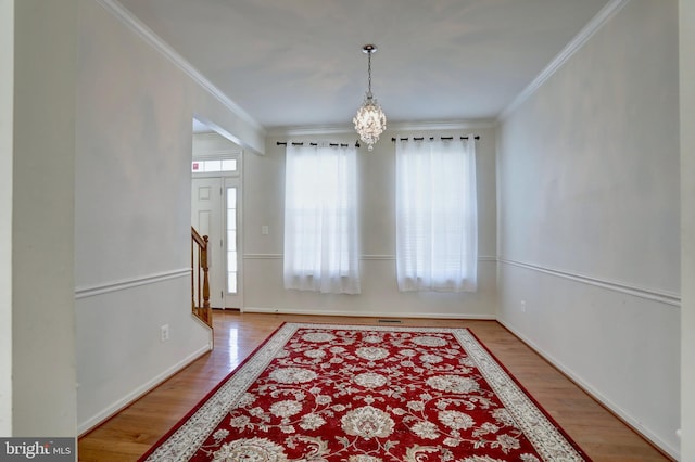 entrance foyer with wood-type flooring, ornamental molding, and a chandelier