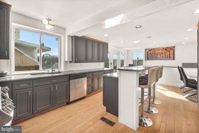 kitchen featuring light hardwood / wood-style floors, dishwasher, a kitchen island, a breakfast bar, and sink