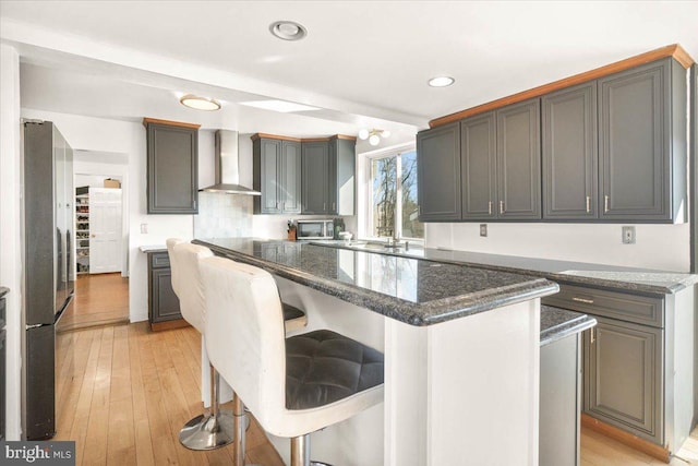 kitchen featuring a kitchen breakfast bar, wall chimney range hood, stainless steel appliances, and a kitchen island