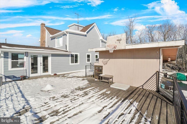 snow covered rear of property with a wooden deck and french doors