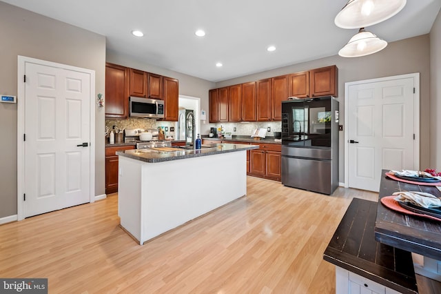 kitchen with light wood-type flooring, pendant lighting, a center island with sink, and appliances with stainless steel finishes