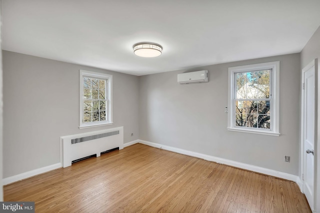 unfurnished room featuring a wall mounted air conditioner, radiator heating unit, and light wood-type flooring