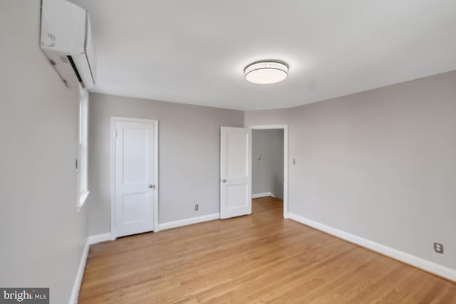 unfurnished bedroom with a wall mounted air conditioner and light wood-type flooring