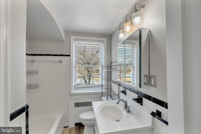 bathroom with toilet, tile walls, vanity, and a tub to relax in