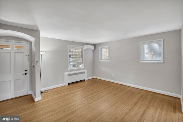 interior space featuring an AC wall unit, radiator heating unit, and light wood-type flooring