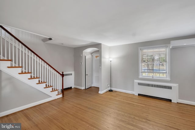 interior space with a wall mounted air conditioner, radiator heating unit, and light wood-type flooring