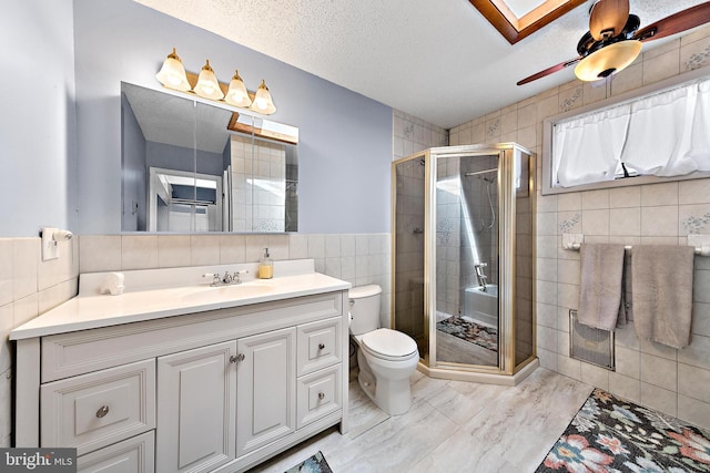 bathroom with ceiling fan, tile walls, a shower with door, and vanity