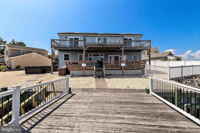 rear view of house featuring a wooden deck, a jacuzzi, and a balcony