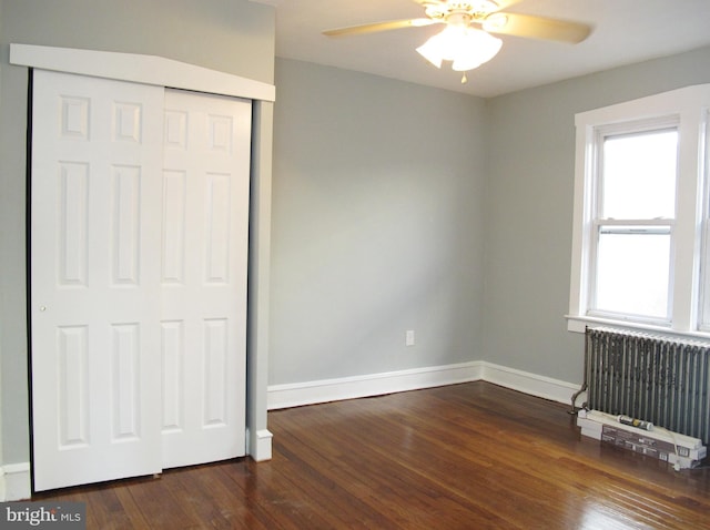 unfurnished bedroom with dark wood-type flooring, ceiling fan, radiator, and a closet