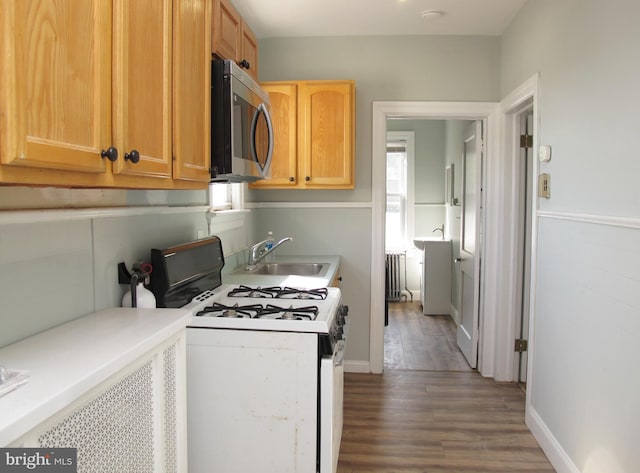 kitchen featuring dark wood-type flooring, white gas range oven, radiator heating unit, and sink