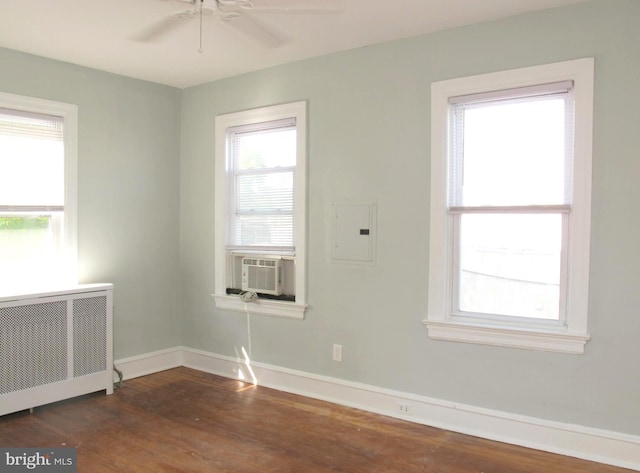 empty room with electric panel, cooling unit, dark hardwood / wood-style flooring, ceiling fan, and radiator heating unit