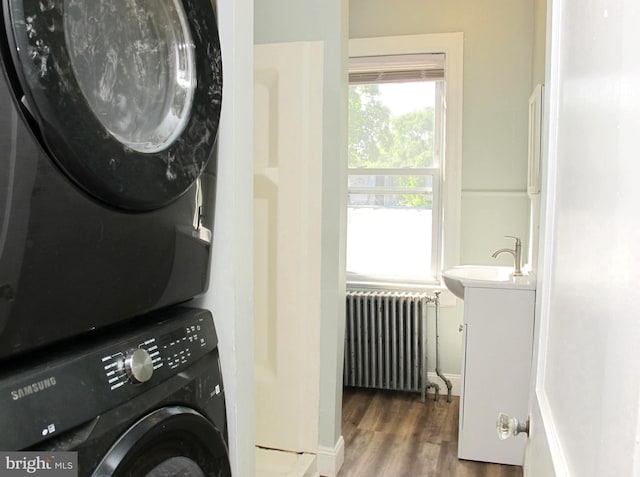 laundry area featuring sink, dark hardwood / wood-style flooring, stacked washer / dryer, and radiator