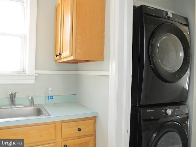 laundry room featuring sink, cabinets, and stacked washer / dryer