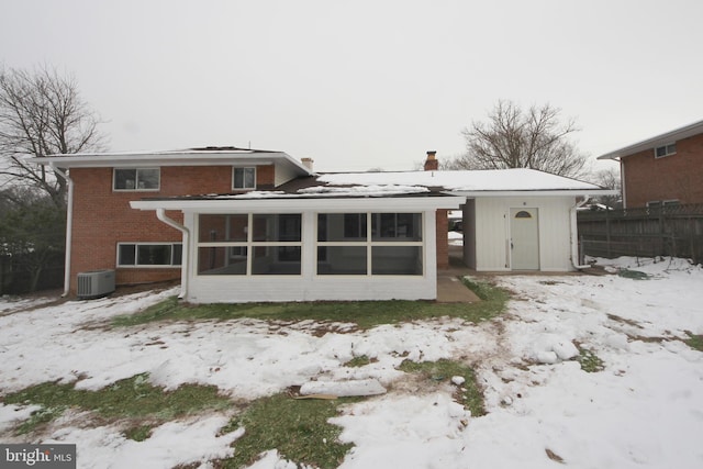 snow covered back of property with central AC unit and a sunroom