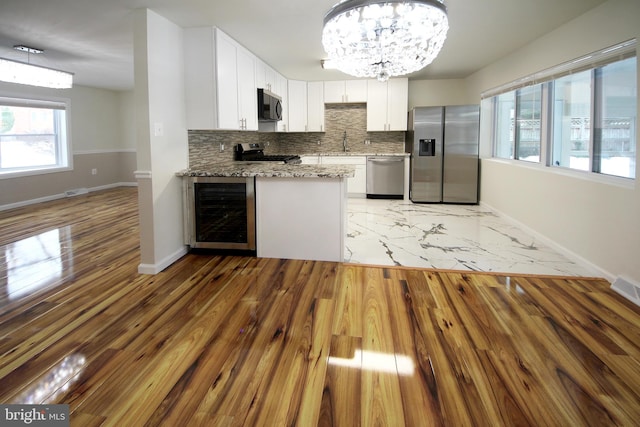 kitchen with light stone countertops, white cabinetry, stainless steel appliances, an inviting chandelier, and wine cooler