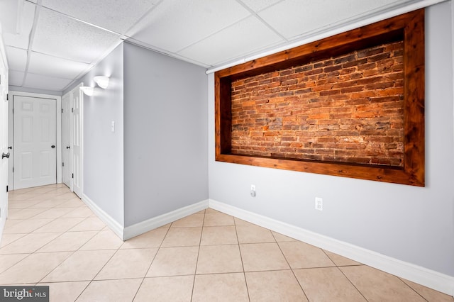 spare room with a paneled ceiling, light tile patterned flooring, and baseboards