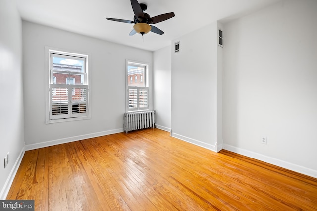 spare room featuring light wood finished floors, baseboards, visible vents, radiator, and ceiling fan