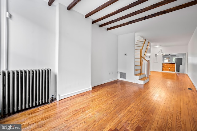 unfurnished living room with visible vents, radiator, hardwood / wood-style flooring, beamed ceiling, and stairs