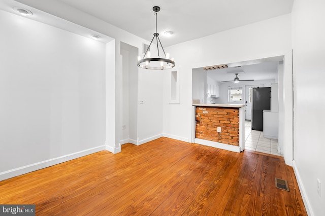 unfurnished dining area featuring light wood finished floors, baseboards, visible vents, and ceiling fan with notable chandelier