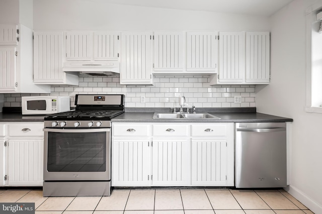 kitchen featuring dark countertops, backsplash, appliances with stainless steel finishes, a sink, and under cabinet range hood