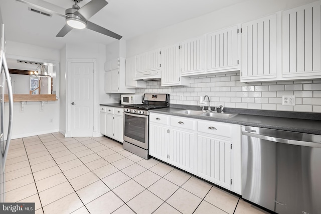 kitchen with stainless steel appliances, dark countertops, a sink, and under cabinet range hood