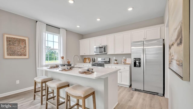 kitchen with a breakfast bar, a kitchen island with sink, white cabinets, appliances with stainless steel finishes, and sink