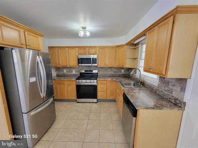 kitchen featuring sink, light tile patterned flooring, tasteful backsplash, and appliances with stainless steel finishes