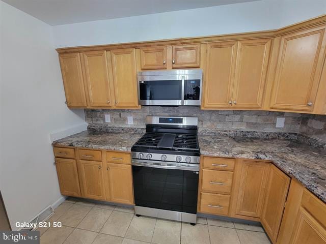 kitchen with backsplash, dark stone counters, appliances with stainless steel finishes, and light tile patterned floors