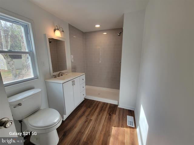 bathroom featuring hardwood / wood-style flooring, a tile shower, a wealth of natural light, and vanity