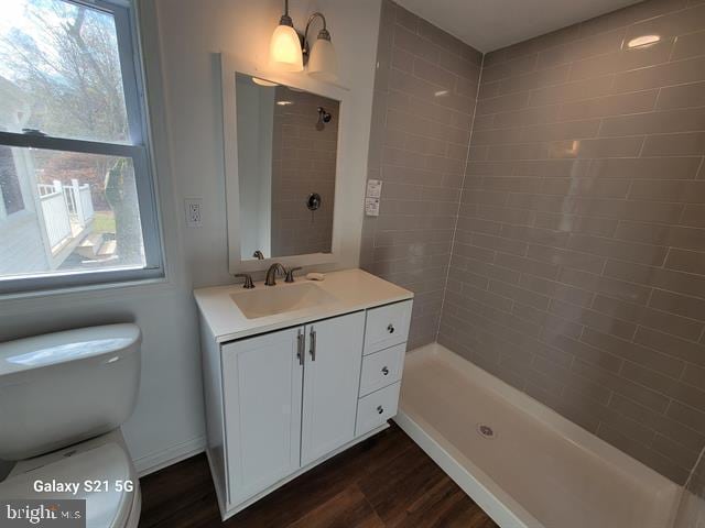 bathroom featuring wood-type flooring, tiled shower, vanity, and toilet