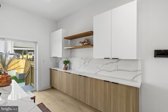 kitchen with white cabinets, light wood-type flooring, light stone countertops, and tasteful backsplash