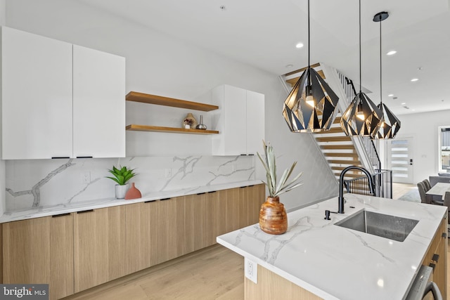 kitchen with light stone countertops, decorative backsplash, sink, white cabinetry, and decorative light fixtures