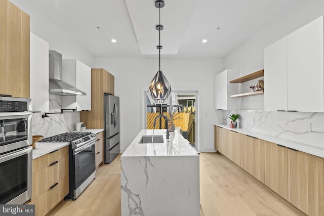 kitchen featuring hanging light fixtures, stainless steel appliances, wall chimney range hood, decorative backsplash, and white cabinetry