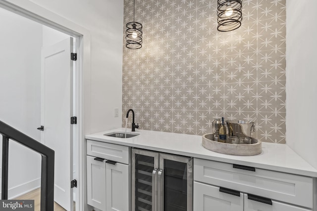 bar with sink, white cabinetry, hanging light fixtures, and wine cooler