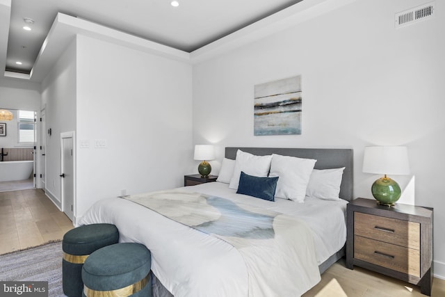 bedroom featuring light wood-type flooring, ensuite bathroom, and a raised ceiling