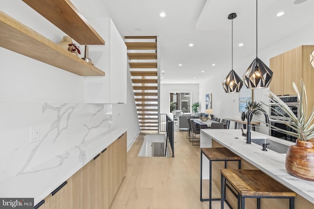 kitchen with a breakfast bar area, hanging light fixtures, light wood-type flooring, light stone countertops, and tasteful backsplash