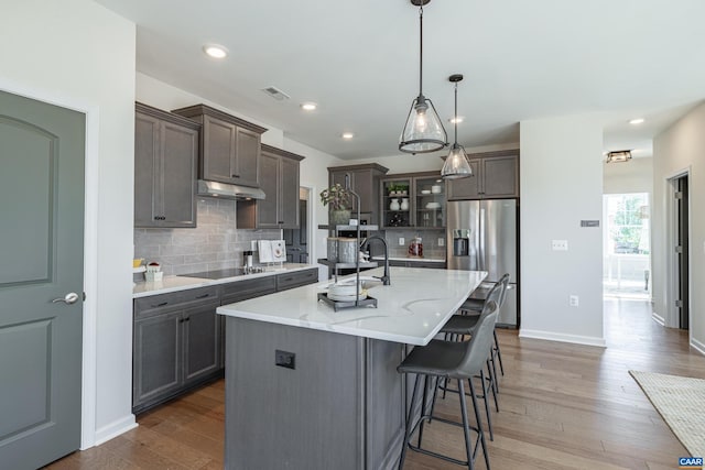 kitchen with pendant lighting, stainless steel refrigerator with ice dispenser, a kitchen island with sink, wood-type flooring, and sink