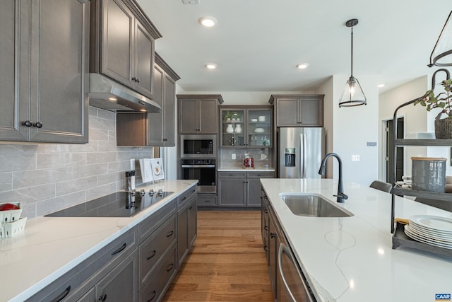 kitchen featuring pendant lighting, stainless steel appliances, decorative backsplash, wood-type flooring, and sink