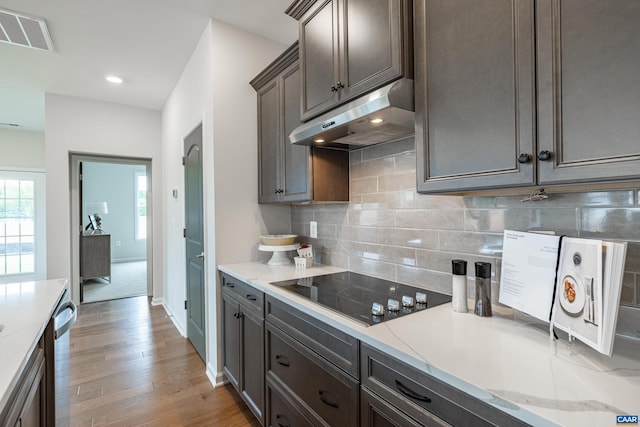 kitchen with light stone countertops, light wood-type flooring, black electric stovetop, and decorative backsplash