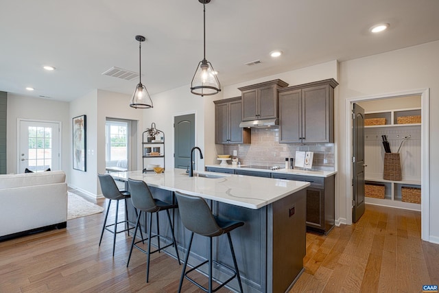 kitchen with decorative light fixtures, a center island with sink, light hardwood / wood-style floors, black electric stovetop, and sink