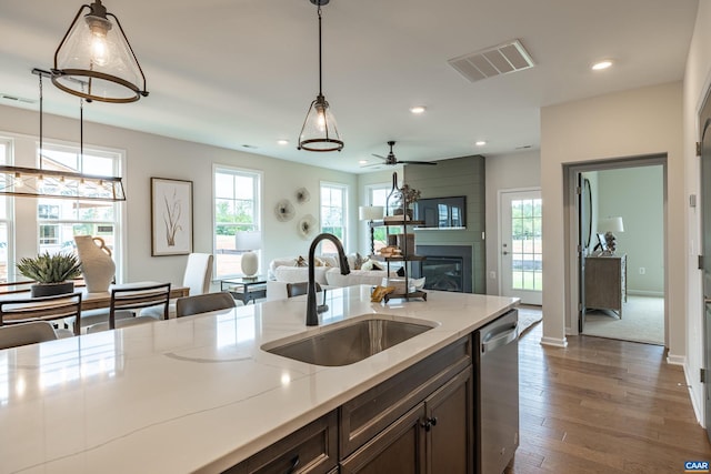 kitchen featuring sink, decorative light fixtures, a large fireplace, stainless steel dishwasher, and light stone countertops