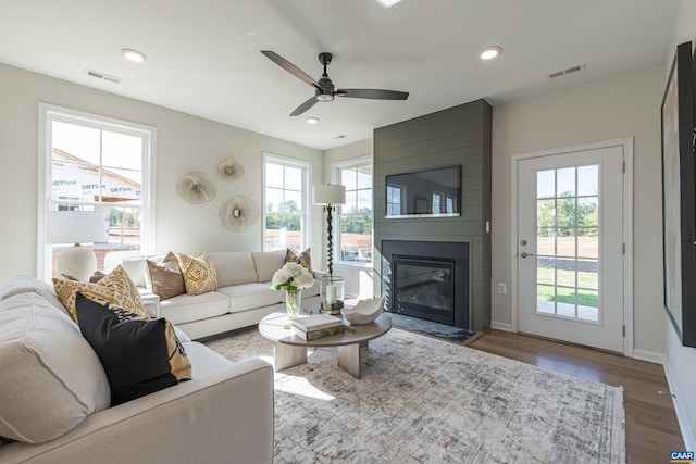 living room featuring wood-type flooring, a large fireplace, ceiling fan, and a healthy amount of sunlight