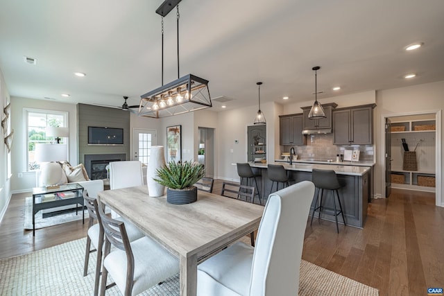 dining space with a fireplace, ceiling fan, and dark wood-type flooring