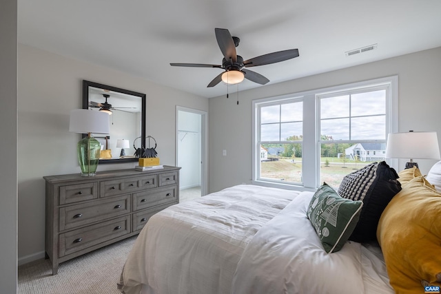 bedroom with a closet, light carpet, ceiling fan, and a spacious closet