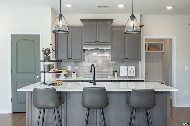 kitchen with light stone countertops, an island with sink, pendant lighting, and sink