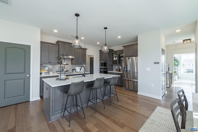 kitchen with a kitchen island with sink, appliances with stainless steel finishes, sink, dark brown cabinets, and decorative light fixtures