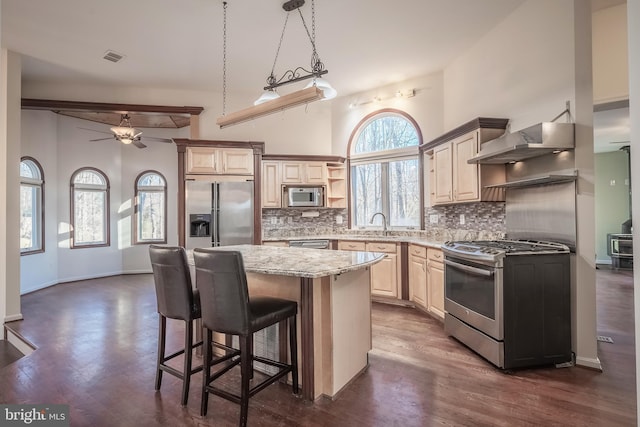 kitchen featuring appliances with stainless steel finishes, a center island, decorative light fixtures, wall chimney range hood, and tasteful backsplash