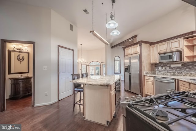 kitchen featuring appliances with stainless steel finishes, light brown cabinets, backsplash, decorative light fixtures, and a center island