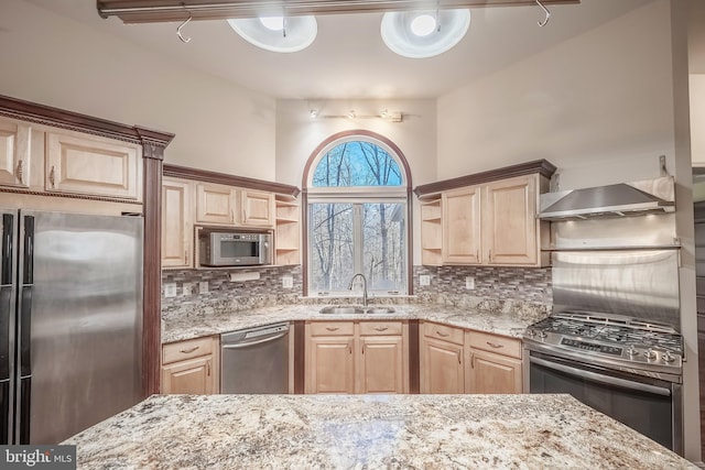 kitchen featuring wall chimney range hood, light brown cabinetry, sink, and stainless steel appliances