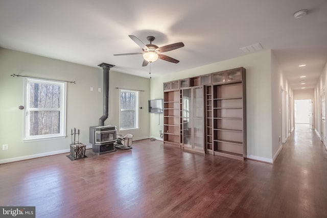 unfurnished living room with dark wood-type flooring, a wood stove, and ceiling fan